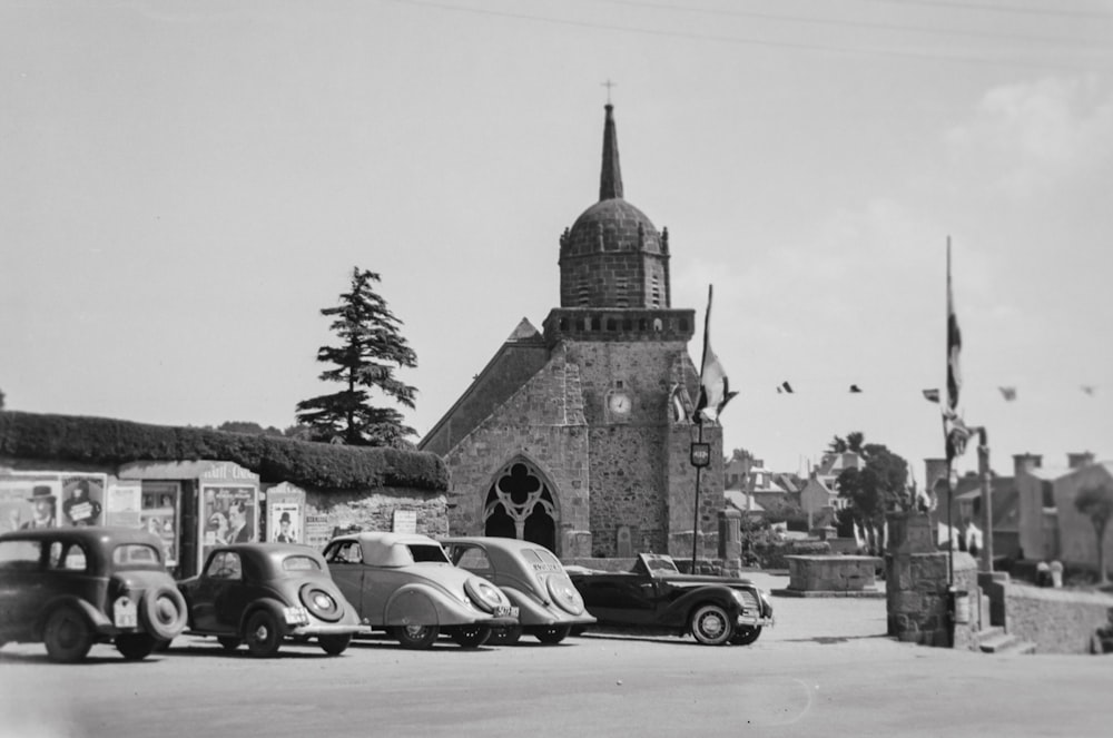 a black and white photo of old cars parked in front of a church