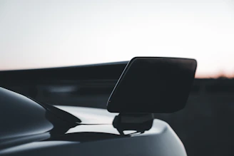Close-up of a sleek black car spoiler mounted on a shiny red sports car under bright sunlight