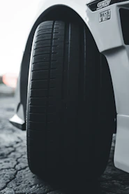 A close-up of a truck tire being photographed by a driver using driverproof on a mobile device, with the truck chassis visible in the background.
