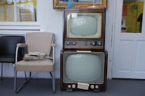 A stack of classic and modern TV show DVDs with a retro television in the background.