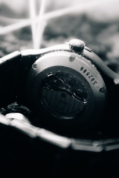 A close-up view of the back of a wristwatch, showcasing intricate mechanical details. The metal casing and visible screws convey a sense of precision engineering, while the blurred background adds depth.