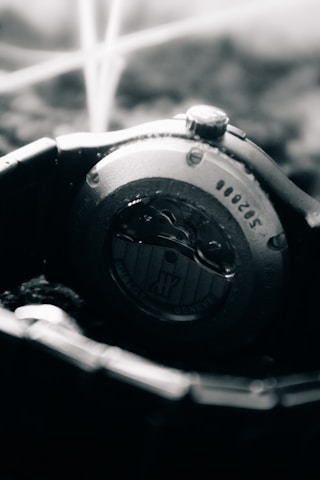 A close-up view of the back of a wristwatch, showcasing intricate mechanical details. The metal casing and visible screws convey a sense of precision engineering, while the blurred background adds depth.
