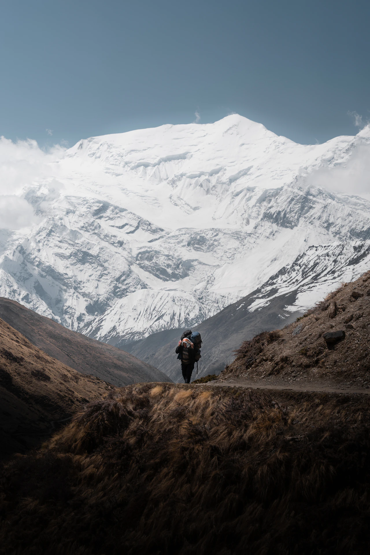 A solitary trekker on a remote Himalayan trail dwarfed by a vast snow-capped Annapurna peak in Nepal