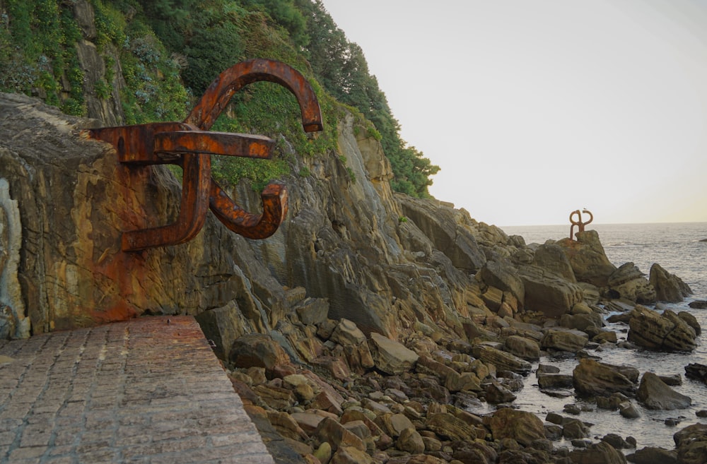 a rusted metal sculpture sitting on the side of a cliff next to the ocean