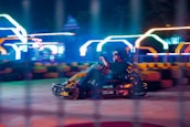 A dynamic shot of a go kart crossing the finish line with orange and black checkered flags waving.