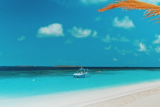 Beautiful tropical beach with clear blue water and a small boat anchored near the shore.