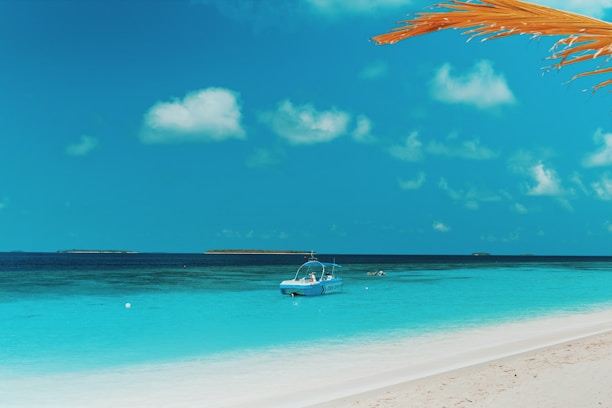 Beautiful tropical beach with clear blue water and a small boat anchored near the shore.