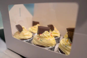 Close-up of a pink cardboard cake box with a transparent window showing a decorated cake inside.