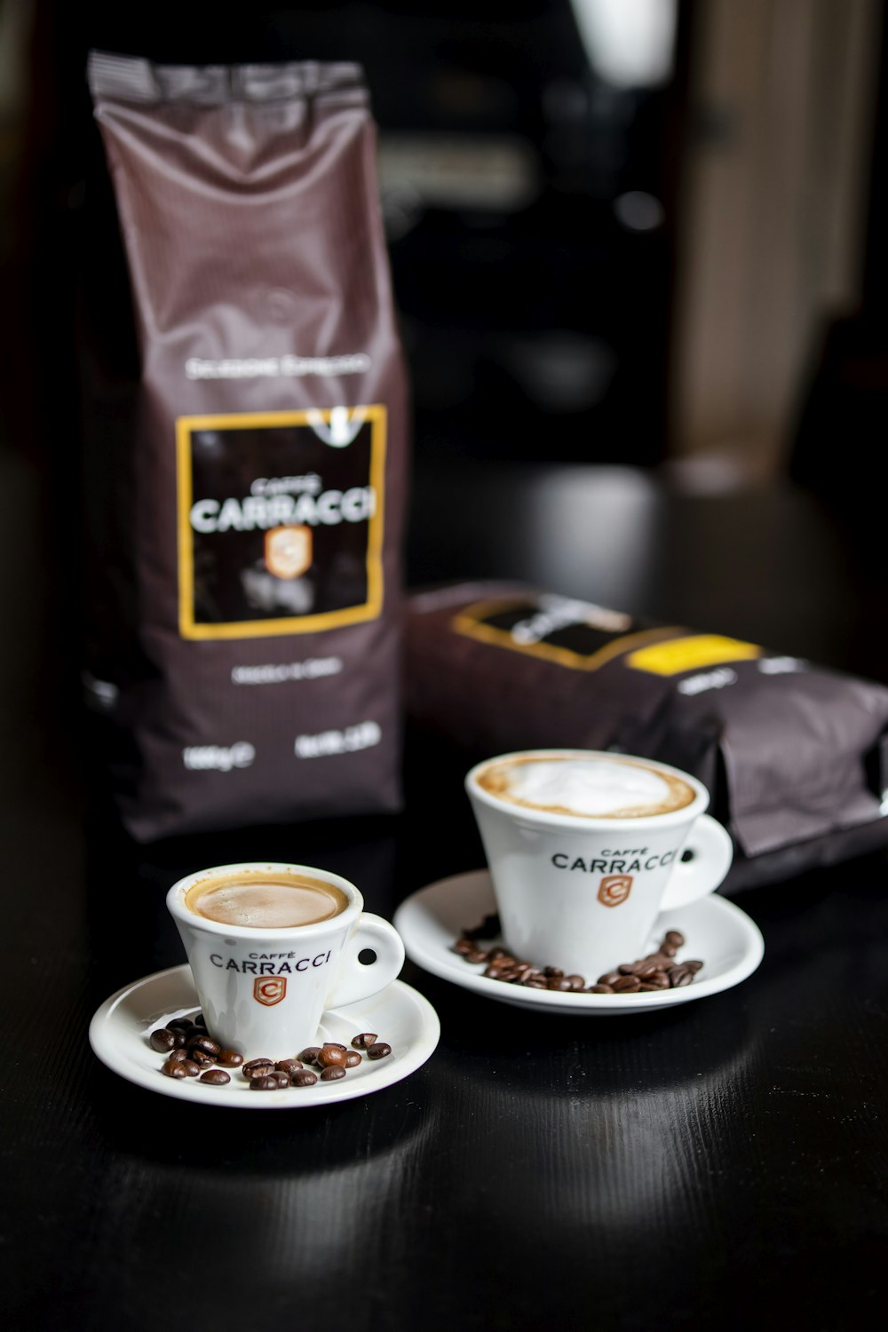 two cups of coffee sit on a table next to a bag of coffee