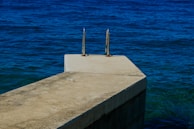 A concrete platform with metal handrails extends out over the deep blue ocean. The texture of the platform contrasts with the smooth surface of the water, which appears vast and calm.