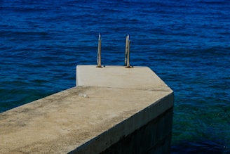 A concrete platform with metal handrails extends out over the deep blue ocean. The texture of the platform contrasts with the smooth surface of the water, which appears vast and calm.