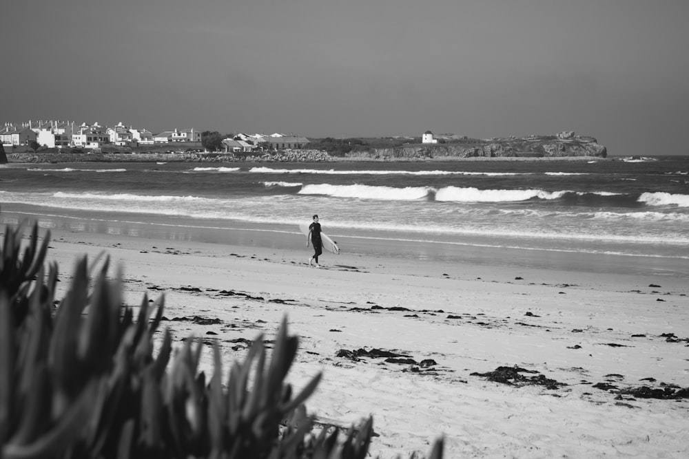 a black and white photo of a person walking on the beach