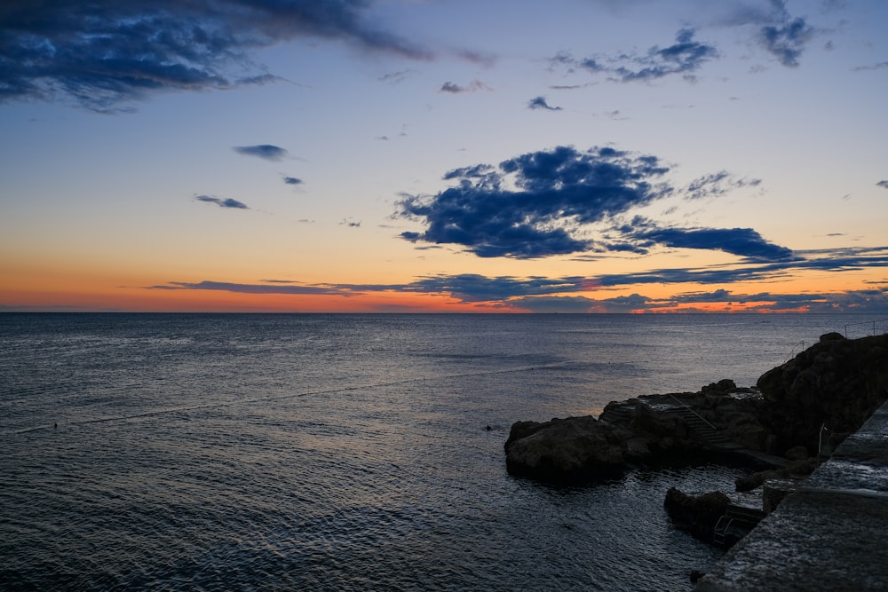 the sun is setting over the ocean with a rock outcropping