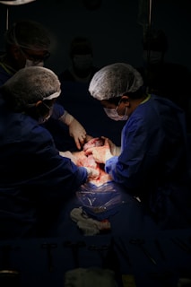 Medical professionals wearing surgical attire perform an operation in a dimly lit operating room. The focus is on the procedure, with surgical instruments and materials nearby.