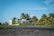 A modern white house is situated on a sandy beach surrounded by lush palm trees under a clear blue sky. The architecture blends seamlessly with the tropical environment, creating a serene and inviting atmosphere.