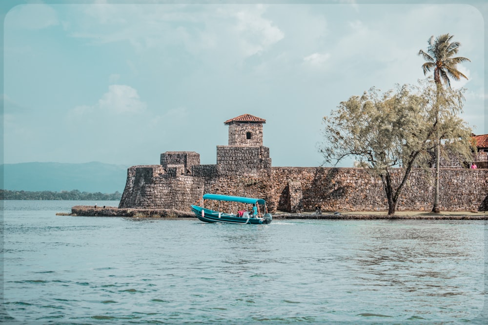 Un barco azul que viaja por un río junto a un muro de piedra