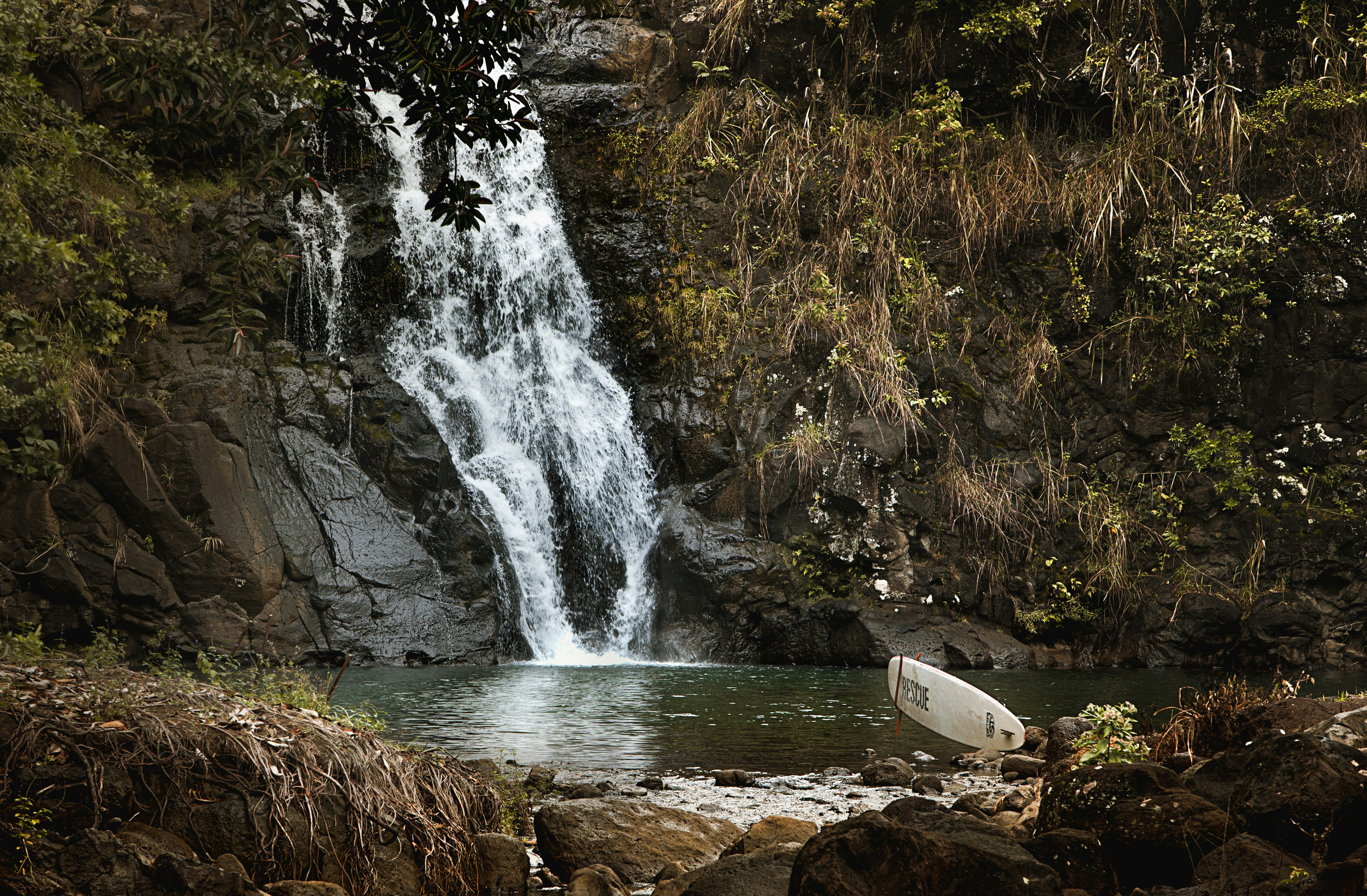 a white surfboard sitting in the water near a waterfall