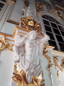 A large, ornate sculpture of an angelic figure with intricately carved wings, set against a lavishly decorated wall featuring golden embellishments and detailed architectural elements.