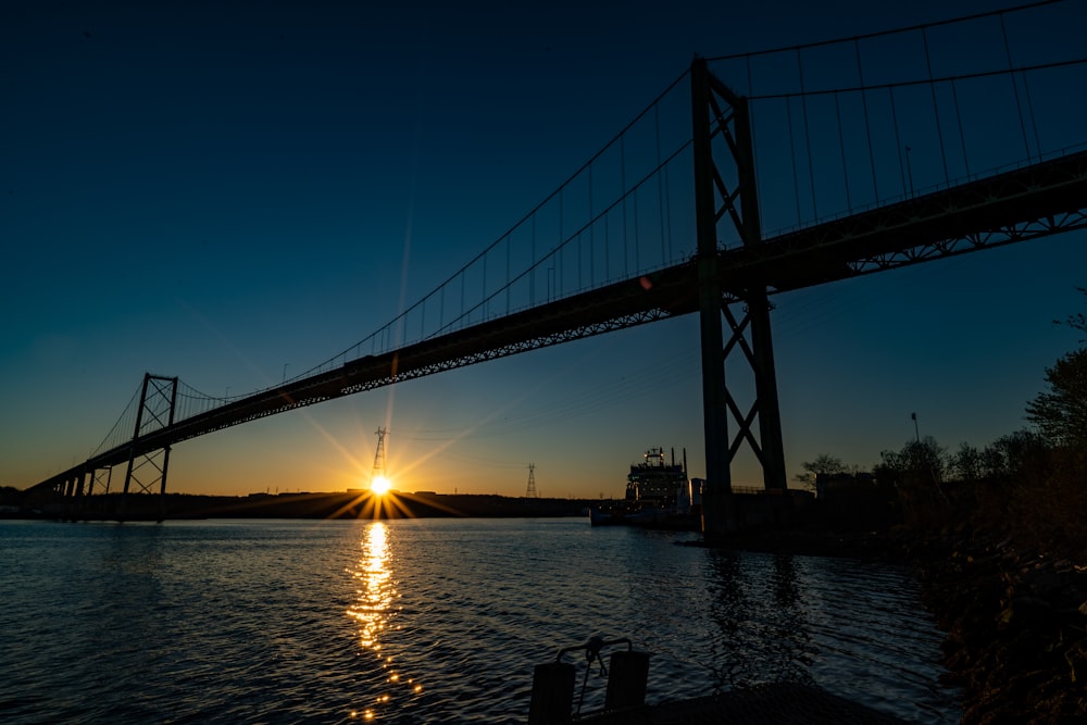 Die Sonne geht hinter einer Brücke über einem Gewässer unter