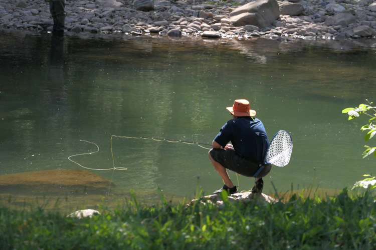angler kneeling by river with a landing net