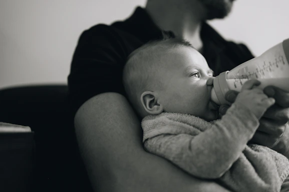 A warm, inviting photo of a child holding a bottle with a smiling caregiver nearby.