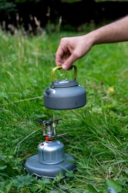 Person carrying a compact propane cylinder outdoors during a camping trip.