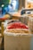 A variety of colorful dried items are displayed in large bags at a bustling market, with a focus on dried citrus slices and red spices. The background is softly blurred, giving a hint of more market stalls and people.