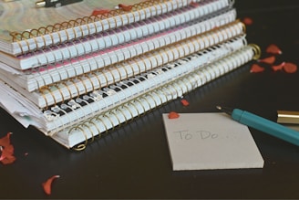 Stack of notebooks and pens with dark floral designs.