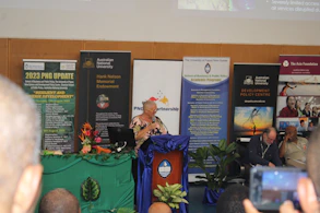 A keynote speaker presenting on stage with the NASWEI banner behind.