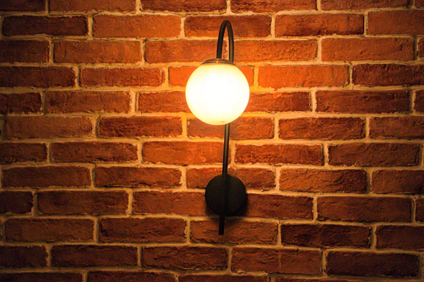 An industrial metal wall sconce mounted on a textured brick wall, casting soft light.