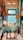 A room filled with musical instruments, predominantly banjos and guitars, arranged on a floor and hung on walls. There is a window with light streaming in, providing a softly lit atmosphere. Various posters and memorabilia add a vintage charm to the setting.