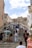 A busy stone staircase with tourists climbing and descending. The architecture is historic, featuring a large stone structure with a clock at the top. Several people are gathered on the steps, some seated and others walking. The scene suggests a vibrant tourist destination.