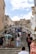 A busy stone staircase with tourists climbing and descending. The architecture is historic, featuring a large stone structure with a clock at the top. Several people are gathered on the steps, some seated and others walking. The scene suggests a vibrant tourist destination.