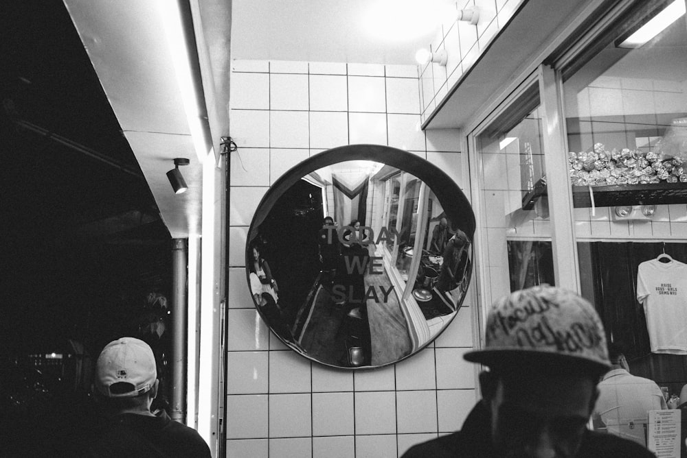 a black and white photo of a man wearing a hat in front of a mirror