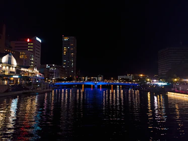 Night cityscape with glowing streetlights and a calm river reflecting the lights.