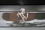 A silver emblem of a prancing horse is mounted on a textured black background, likely the badge of a luxury sports car.