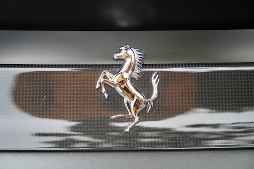 A silver emblem of a prancing horse is mounted on a textured black background, likely the badge of a luxury sports car.