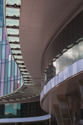 An architectural image featuring curved and sleek building elements with reflective glass panels. The design incorporates smooth, flowing lines and a modern aesthetic. The buildings exhibit a complex interplay of light and shadow.