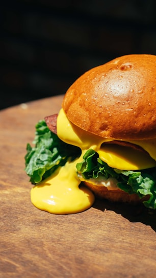 Close-up of a gourmet burger with fresh lettuce and melted cheese on a rustic wooden table.