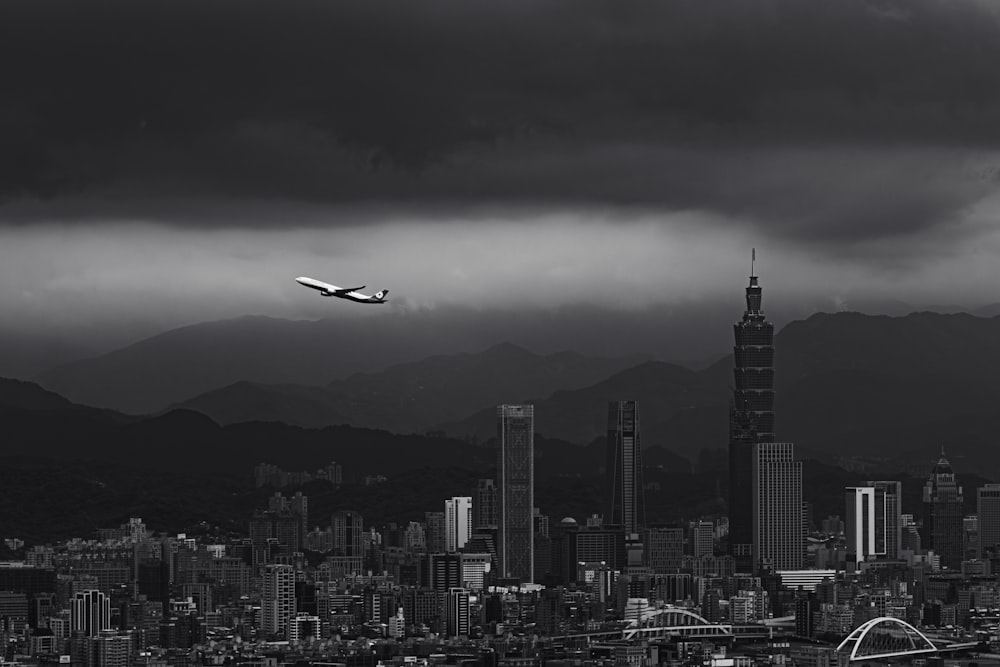 a black and white photo of a plane flying over a city