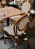 A rattan dining chair with soft cushions placed next to a small, round outdoor table.