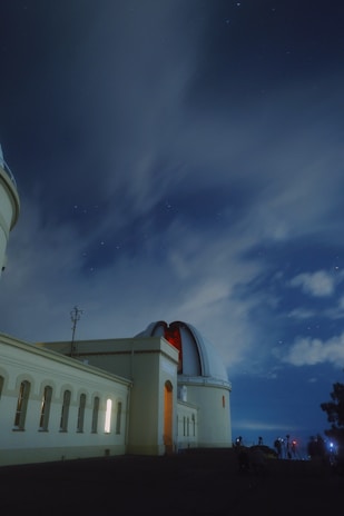 A modern observatory dome illuminated under a clear night sky filled with stars.