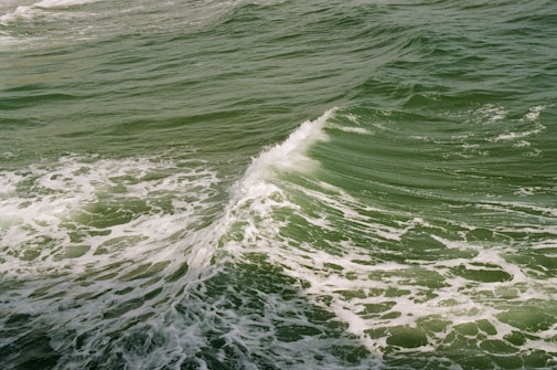 A dynamic ocean scene with green waves crashing and white foam forming intricate patterns on the water's surface.