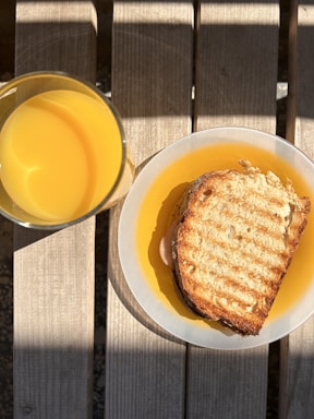 A rustic wooden table with a variety of fresh breakfast sandwiches and a glass of orange juice, sunlight streaming in.