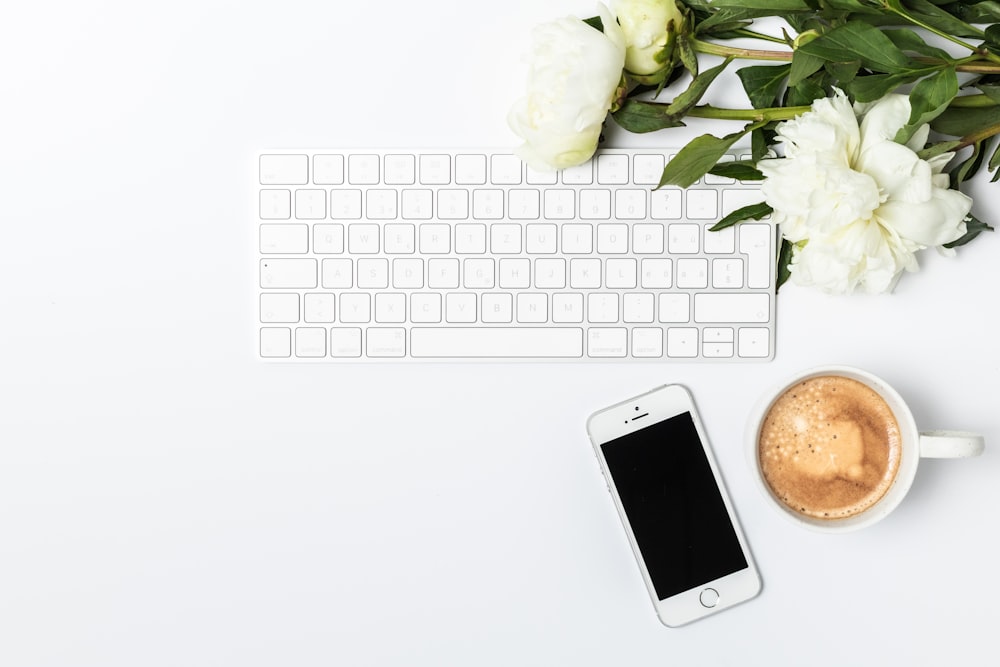 a cup of coffee next to a keyboard and a phone
