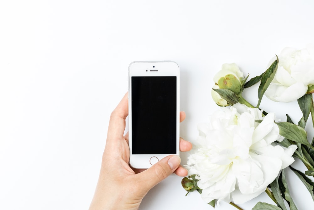 a person holding a cell phone next to a bouquet of flowers