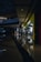 A shopping mall corridor is shown with dim lighting, reflective polished floors, and modern architectural elements. On the right side, a brightly lit storefront labeled 'POP MART' stands out, attracting some people inside. The ceiling features recessed lighting and architectural curves, while reflections of lights on the floor add a visual depth.