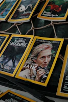 Several National Geographic magazines are laid out in a display, showcasing covers with striking images of wildlife and iconic figures. One cover prominently features a person holding binoculars, hinting at themes of exploration and nature.
