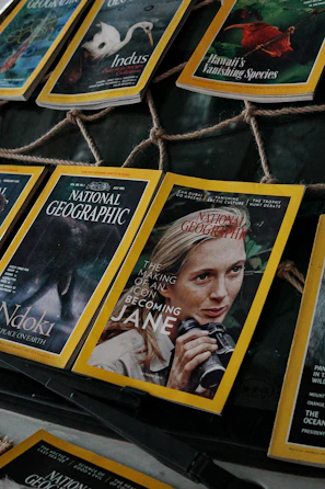 Several National Geographic magazines are laid out in a display, showcasing covers with striking images of wildlife and iconic figures. One cover prominently features a person holding binoculars, hinting at themes of exploration and nature.