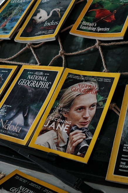 Several National Geographic magazines are laid out in a display, showcasing covers with striking images of wildlife and iconic figures. One cover prominently features a person holding binoculars, hinting at themes of exploration and nature.